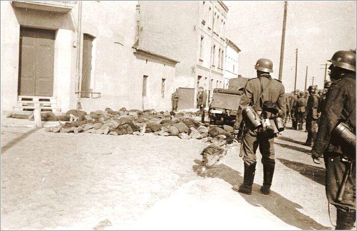 German soldiers stand guard on a street in Czestochowa, where the bodies of Jewish men they have shot lie on the pavement.